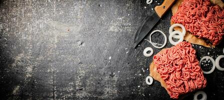 Fresh minced meat on paper on a table with a knife and onion rings. photo