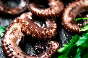 Pieces of fresh octopus on a stone board with greenery. photo