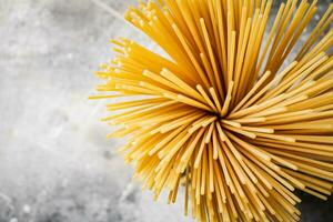 A bundle of spaghetti dry tied with a rope stands on the table. photo