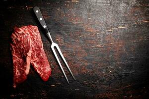 Raw steak with a large fork on the table. photo