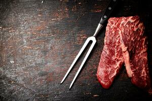 Raw steak with a large fork on the table. photo