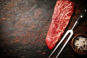 Raw steak with a large fork on the table. photo