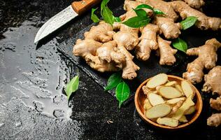 Pieces and whole ginger on a stone board with foliage. photo