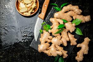 Pieces and whole ginger on a stone board with foliage. photo