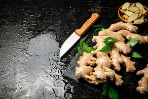 Pieces and whole ginger on a stone board with foliage. photo