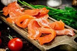 Slices of salted salmon on a cutting board with dill and tomatoes. photo