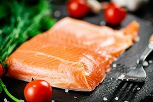 A piece of salted salmon with tomatoes and greens on a stone board. photo