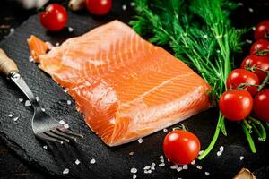 A piece of salted salmon with tomatoes and greens on a stone board. photo