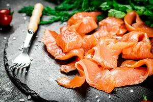 piezas de salado salmón con verdor en un Roca tablero. foto