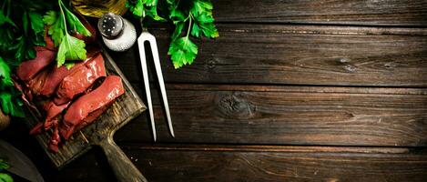 Pieces of raw liver on a cutting board with parsley and spices. photo