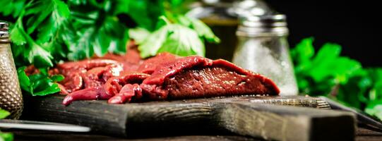 Pieces of raw liver on a cutting board with parsley and spices. photo