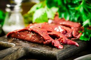 Pieces of raw liver on a cutting board with parsley and spices. photo