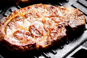 Grilled pork steak in a frying pan. Macro background. photo