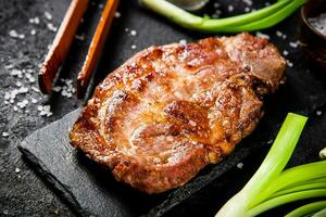Grilled pork steak on a stone board with green onions and spices. photo