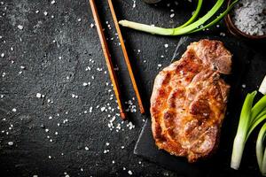 Grilled pork steak on a stone board with green onions and spices. photo