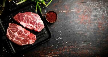 Raw pork steak in a frying pan with green onions and spices. photo