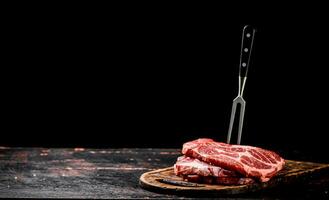 Raw pork steak on a cutting board with fork. photo