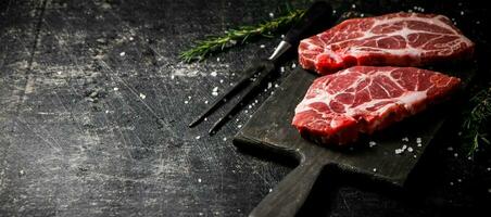 Raw pork steak on a cutting board with rosemary. photo