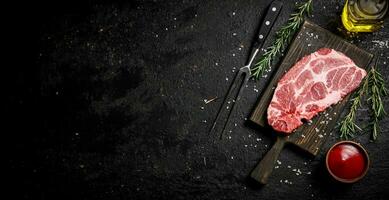 A steak of raw pork on a cutting board with tomato sauce and rosemary. photo