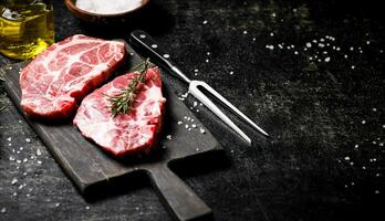 Raw pork steak on a cutting board with rosemary. photo