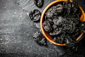 Prunes in a wooden plate on a stone board. photo