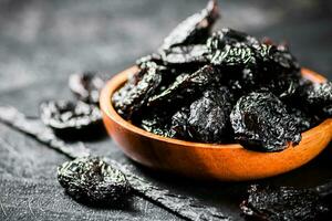 Prunes in a wooden plate on a stone board. photo