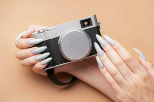 Woman's hand with grey nail polish holding camera photo