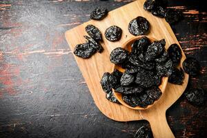 Prunes in a plate on a wooden cutting board. photo