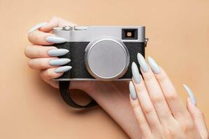 Woman's hand with grey nail polish holding camera photo