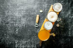 Different glasses of beer on a wooden cutting Board with opener. photo