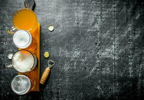 Different glasses of beer on a wooden cutting Board with opener. photo