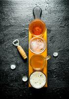 Various glasses of beer on a wooden cutting Board with opener. photo