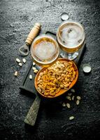 Two glasses of beer and peanuts in a bowl on a black cutting Board. photo