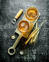 Two glasses of beer on a stand with spikelets and opener. photo