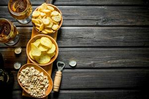 Beer and various kinds of snacks in the bowls on the cutting Board. photo