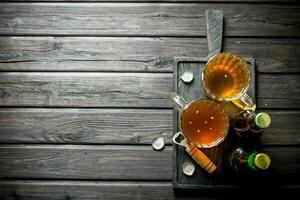 Beer in mugs and bottles with opener on the cutting Board. photo