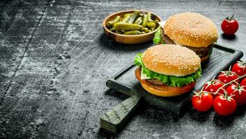 Burgers on a cutting Board with tomatoes and gherkins in a bowl. photo