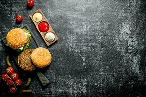 Burgers with French fries, gherkins,tomatoes and different sauces. photo