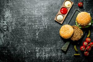 Burgers with French fries, gherkins,tomatoes and different sauces. photo