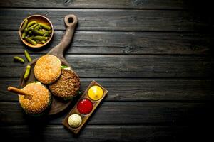 Burgers on a cutting Board with a knife and gherkins in a bowl. photo