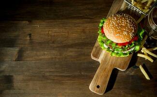 hamburguesa en un corte tablero con cerveza y papas fritas foto