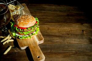 hamburguesa en un corte tablero con cerveza y papas fritas foto