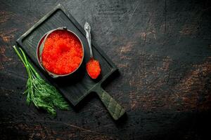Red caviar in a bowl and a spoon on a cutting Board with dill. photo