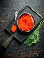 Red caviar in a bowl and a spoon on a cutting Board with dill. photo