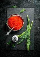 Red caviar in a bowl on a black stone Board with salt and dill. photo