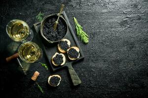 emparedados con negro caviar, caviar en un cuenco y blanco vino. foto