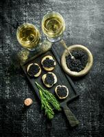 Black caviar in a bowl and sandwiches with caviar on a cutting Board with dill and white wine. photo