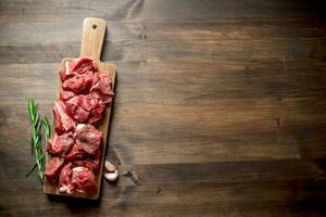 cortar crudo carne de vaca en un de madera corte tablero con Romero y ajo. foto