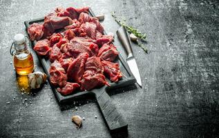 Cut raw beef on a cutting Board with a knife, thyme and oil in the bottle. photo