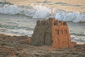castillo de arena en el antecedentes de el mar durante un puesta de sol a vacaciones foto